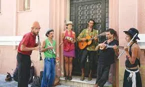 A street band of seven musicians with clarinets, guitar, mandolin and percussion plays in front of a doorway