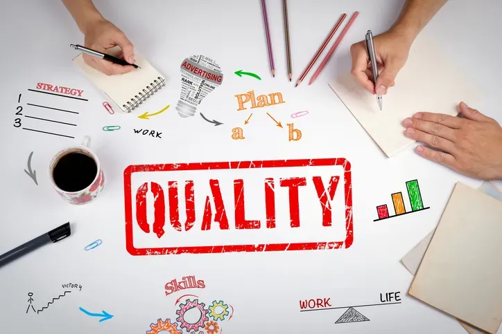 Hands writing on notepads around the word 'Quality' stamped in red, surrounded by doodles of strategy, plan, skills and work-life balance