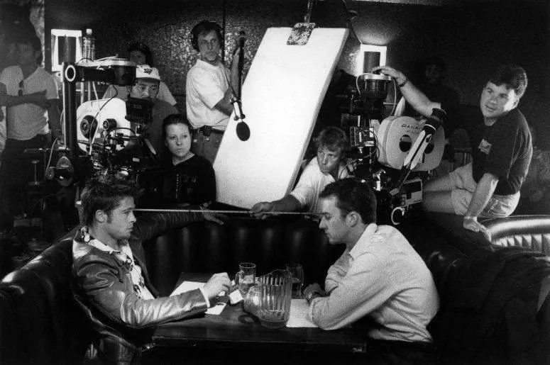 Black and white behind-the-scenes photo of a crew with cameras, a boom mic and a bounce board filming two actors in a diner booth