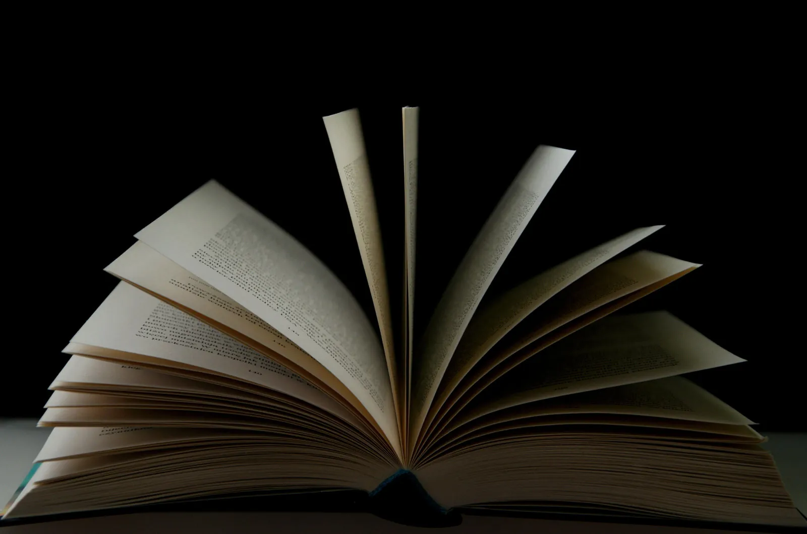 An open book with its pages fanned upward against a black background